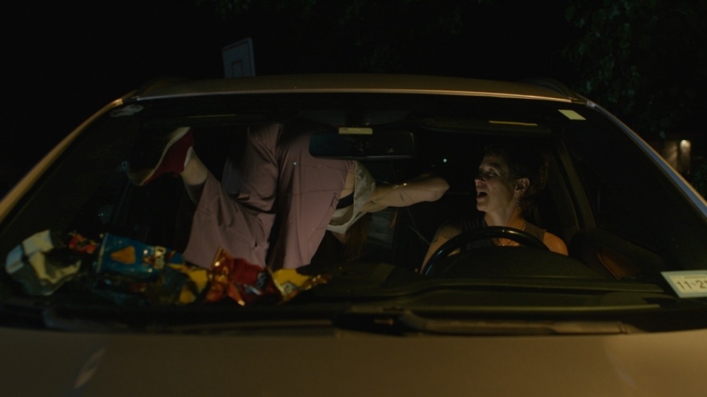 lily leans over the front seat of a car next to emma