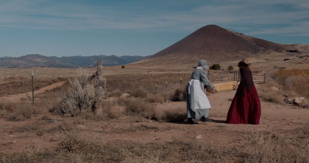 emma and lily carry a suitcase together toward a mountain